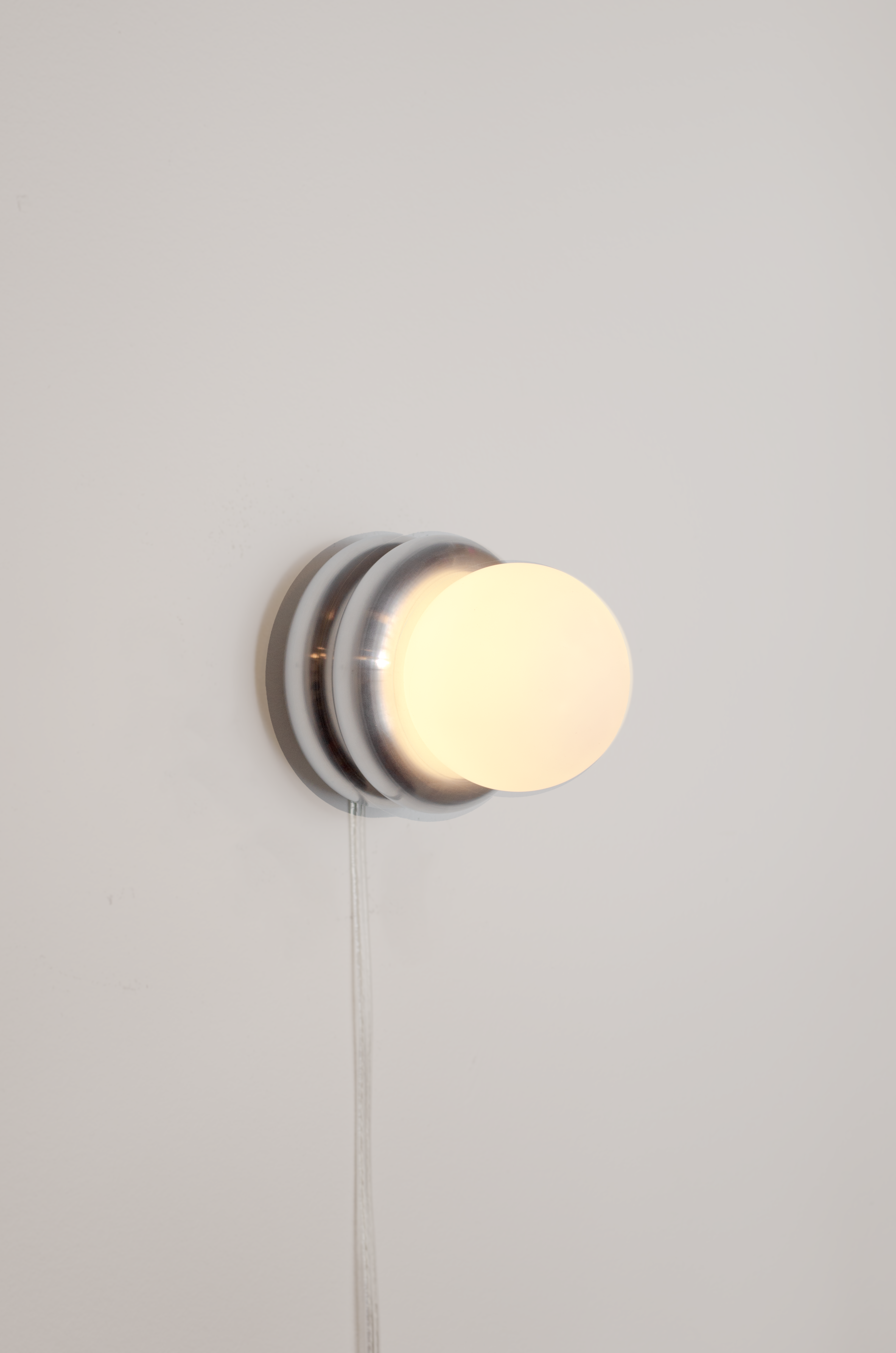 Donut wall lamp by HAHA studio. A compact lamp made of two stacked aluminum donut shapes, displayed on the wall.