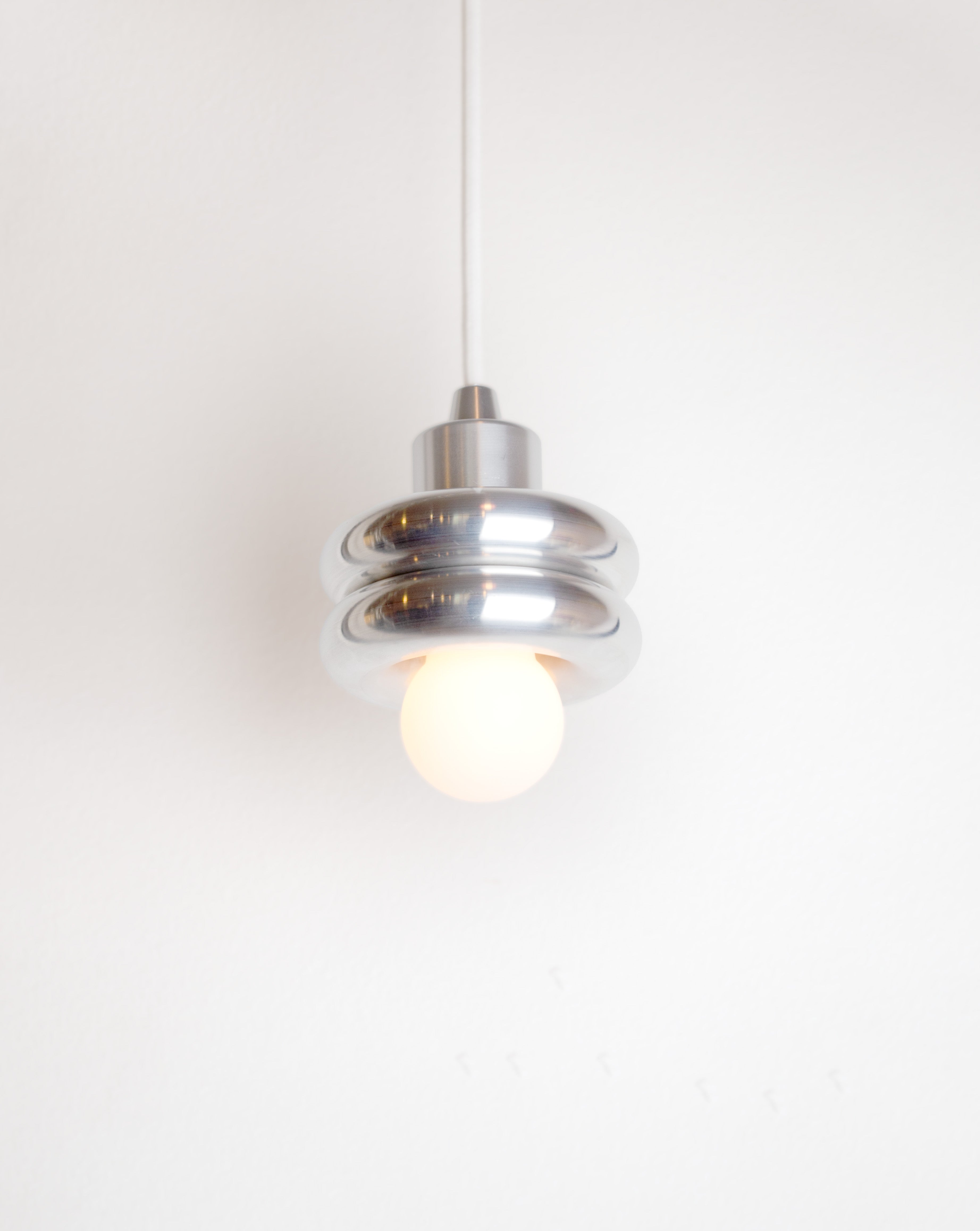 Donut pendant lamp by HAHA studio. A compact lamp made of two stacked aluminum donut shapes.